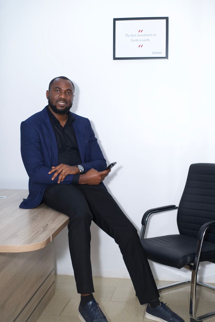 Confident businessman seated on a desk in a modern office, holding a phone.